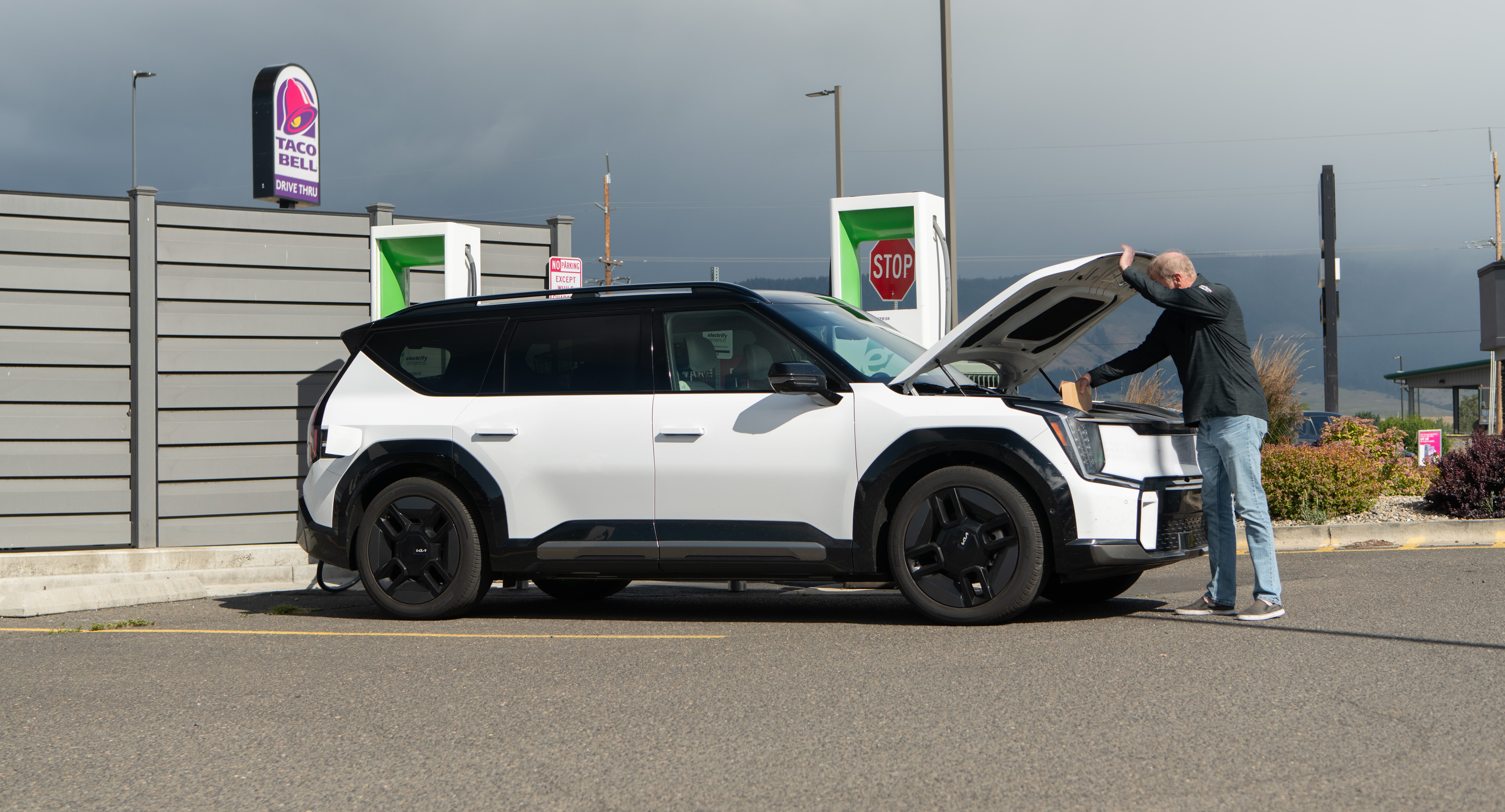 Man standing next to his EV with open bonnet waiting for it to charge