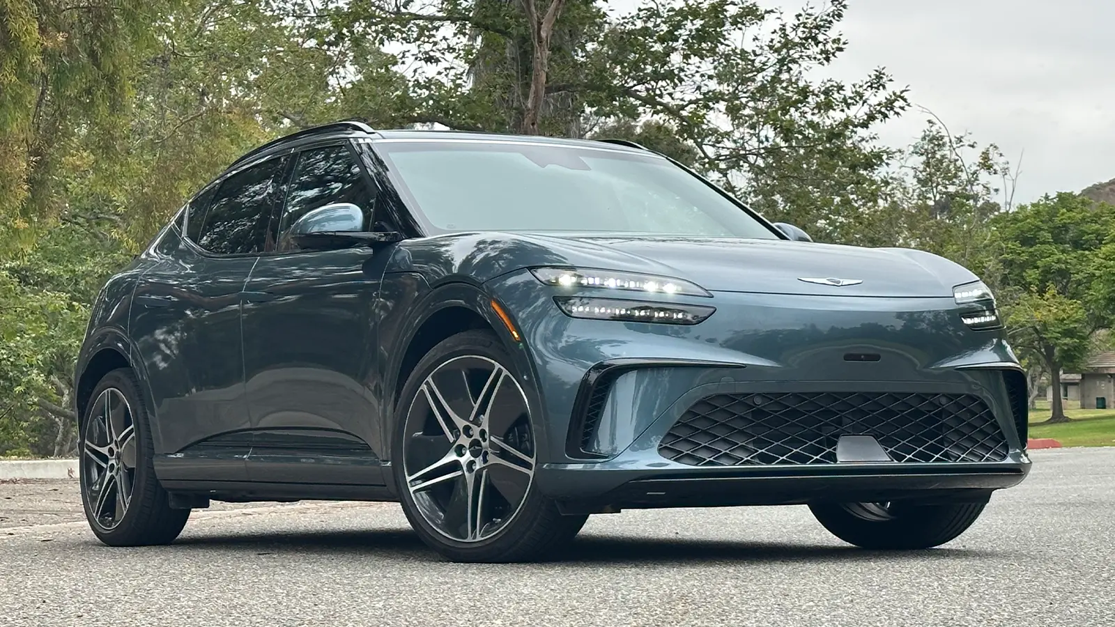 A 2026 dark blue Genesis GV60 three quarter front view in the forest