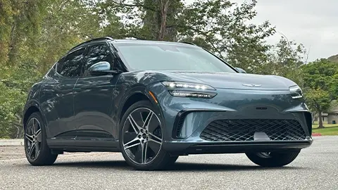 A 2026 dark blue Genesis GV60 three quarter front view in the forest