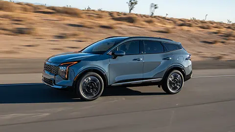 Vista frontal de tres cuartos de un Kia Sportage 2026 gris oscuro circulando por una autopista junto a un desierto