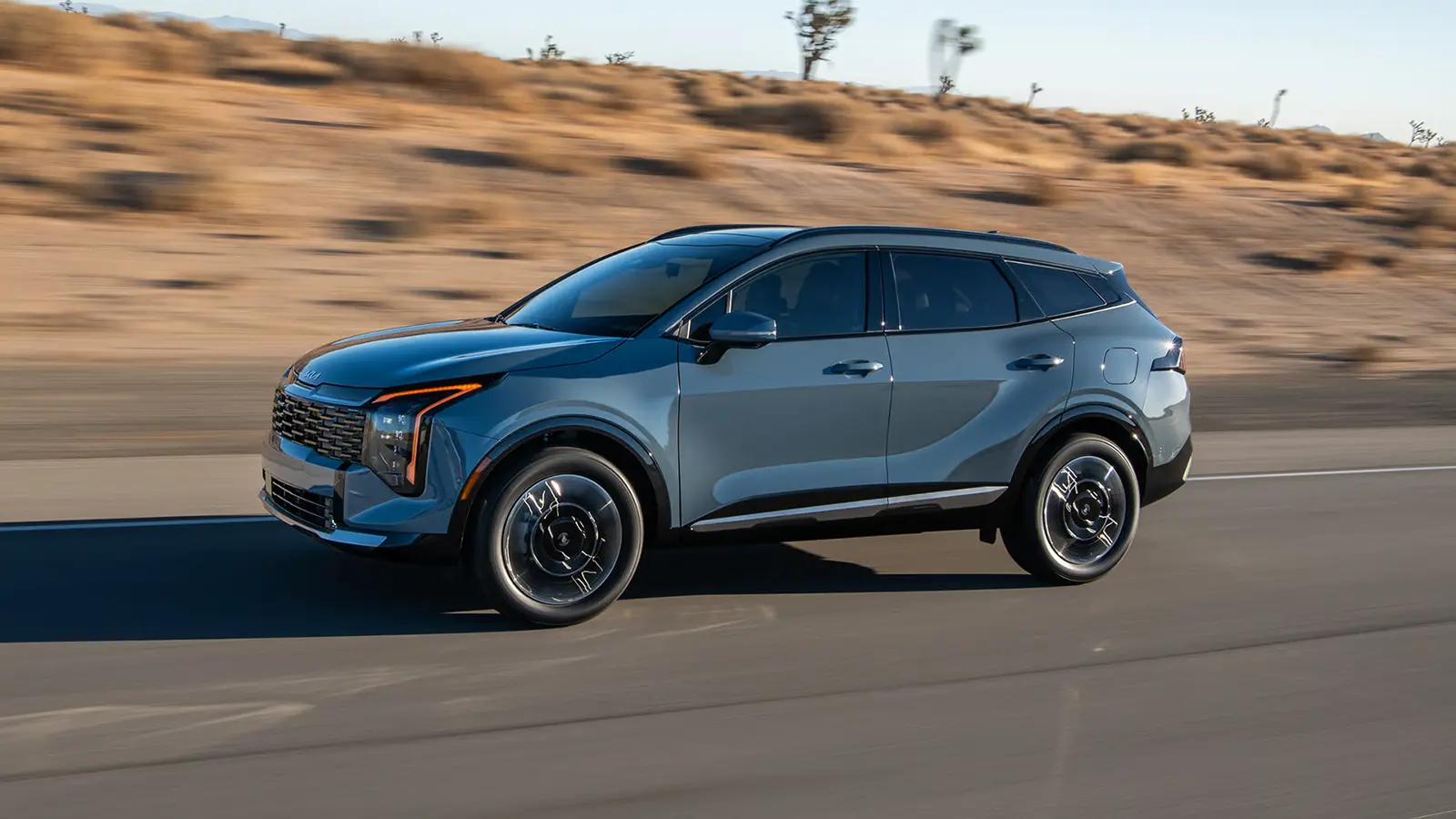 A dark gray 2026 Kia Sportage three quarter front view being driven on the highway next to a desert