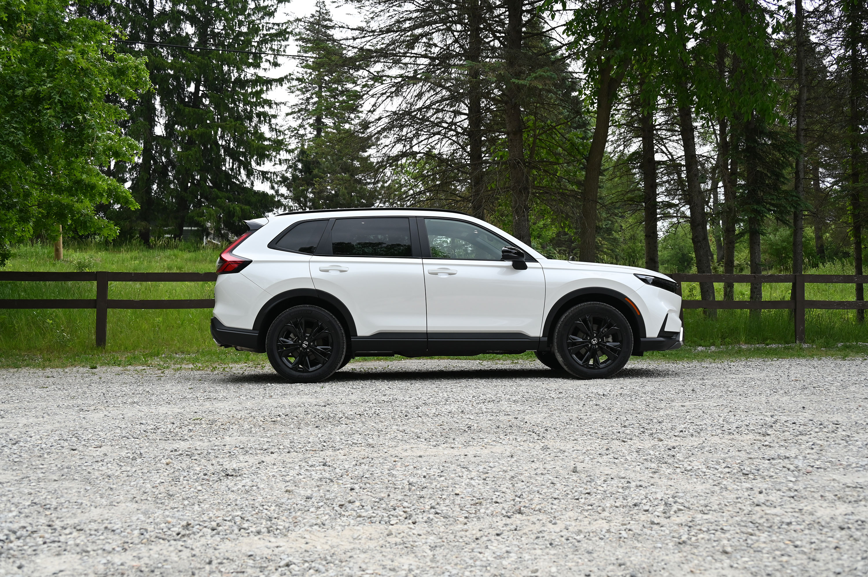 White 2026 Honda CR-V Hybrid Sport standing next to a fence