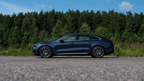 A dark blue 2027 Mercedes-Benz C400 4MATIC Electric staged in front of a dense green pine forest