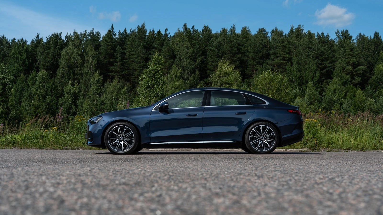 A dark blue 2027 Mercedes-Benz C400 4MATIC Electric staged in front of a dense green pine forest