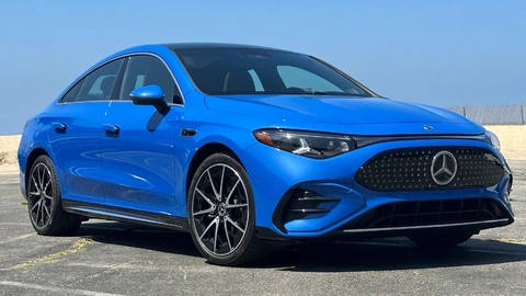 A blue 2027 Mercedes-Benz CLA 250+ Electric angled on pavement in front of a beach and blue skies