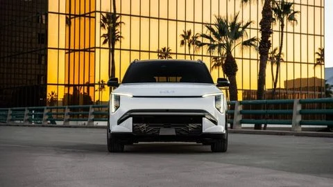 A white 2027 Kia EV3 front profile sitting in front of an office building with mirrored windows and palm trees