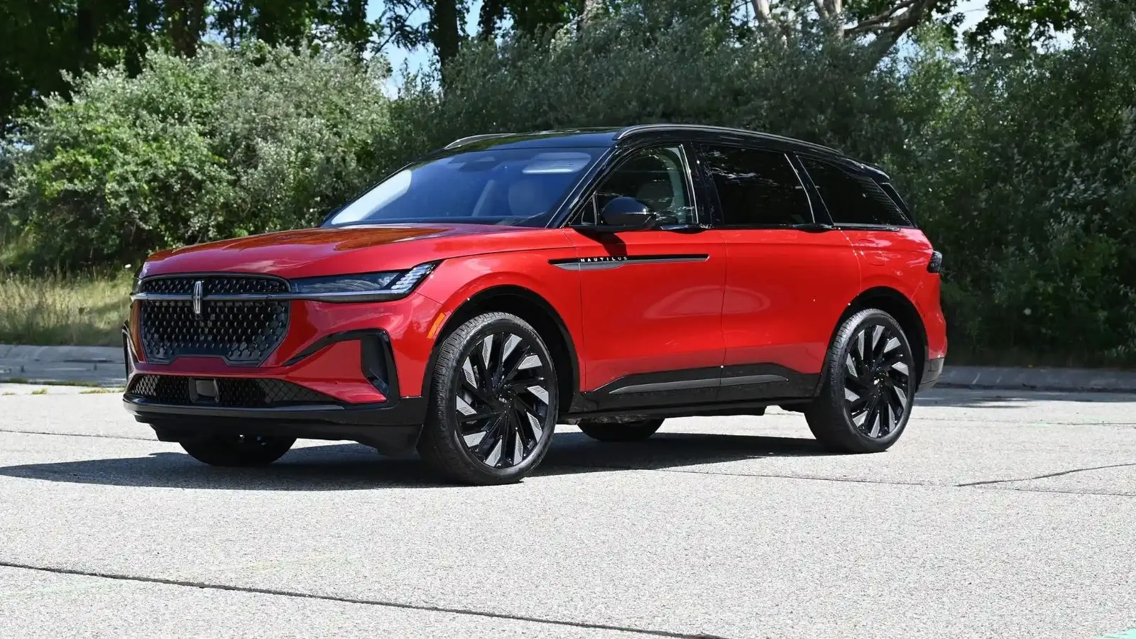 Angled front image of a red 2026 Lincoln Nautilus Hybrid in a parking lot in front of a wooded area