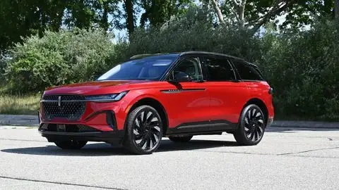 Angled front image of a red 2026 Lincoln Nautilus Hybrid in a parking lot in front of a wooded area