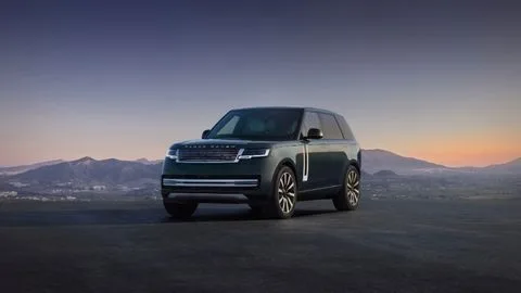 El Range Rover eléctrico 2027 aparcado frente a un terreno montañoso mientras sale el sol por el horizonte