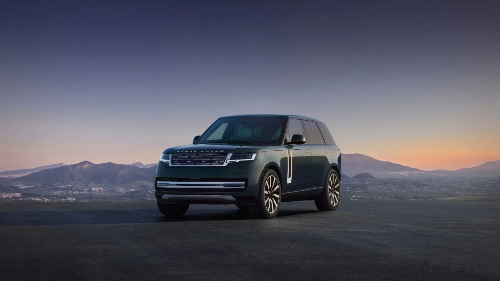 El Range Rover eléctrico 2027 aparcado frente a un terreno montañoso mientras sale el sol por el horizonte