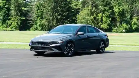2026 Hyundai Elantra Hybrid parked in an empty parking lot on an angle in front of green grass and a heavily forested area