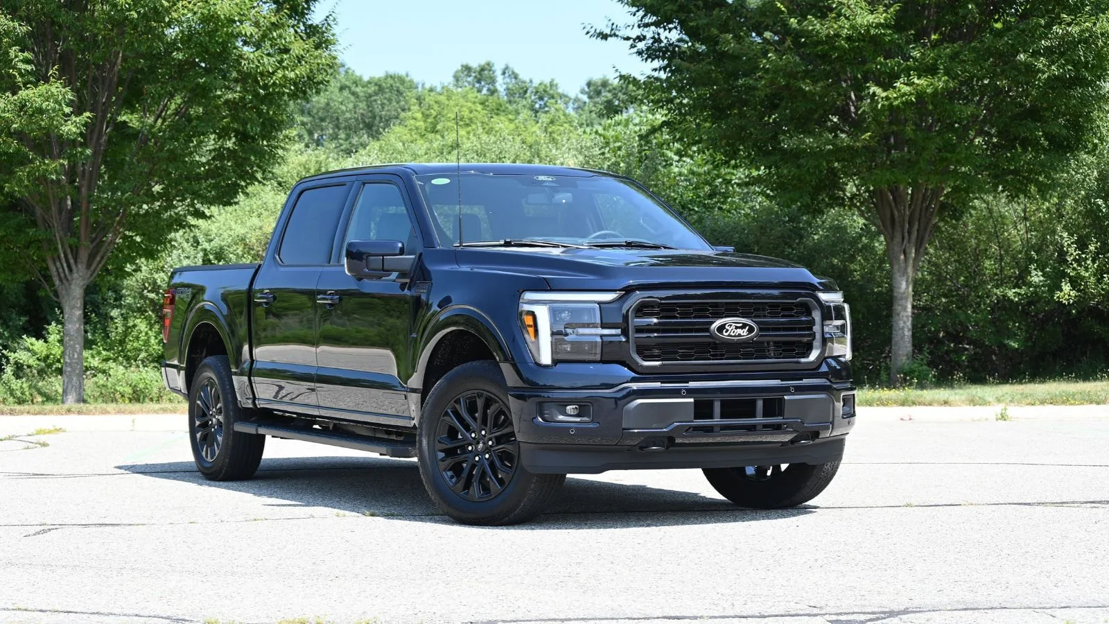 A 2026 Ford F-150 Powerboost Hybrid is parked at an angle in a parking lot against a landscaped background