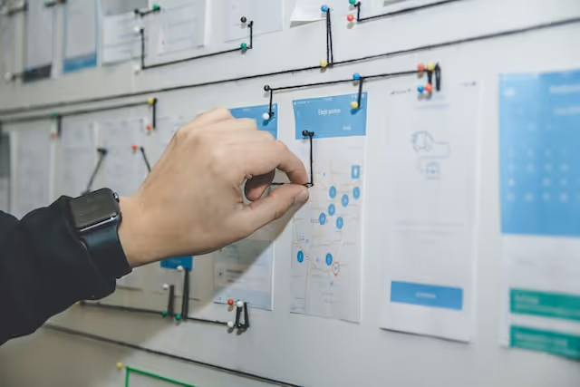 Person with a smartwatch adjusting pinned papers on a board filled with documents and connected strings.