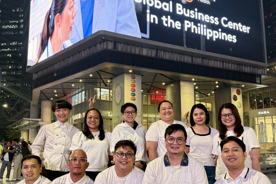Tenet ve Conifer Global Business Center ekip üyeleri, Taguig'deki BGC High Street'te “A Global Business Center in the Philippines” yazan Tenet Health ekranının önünde