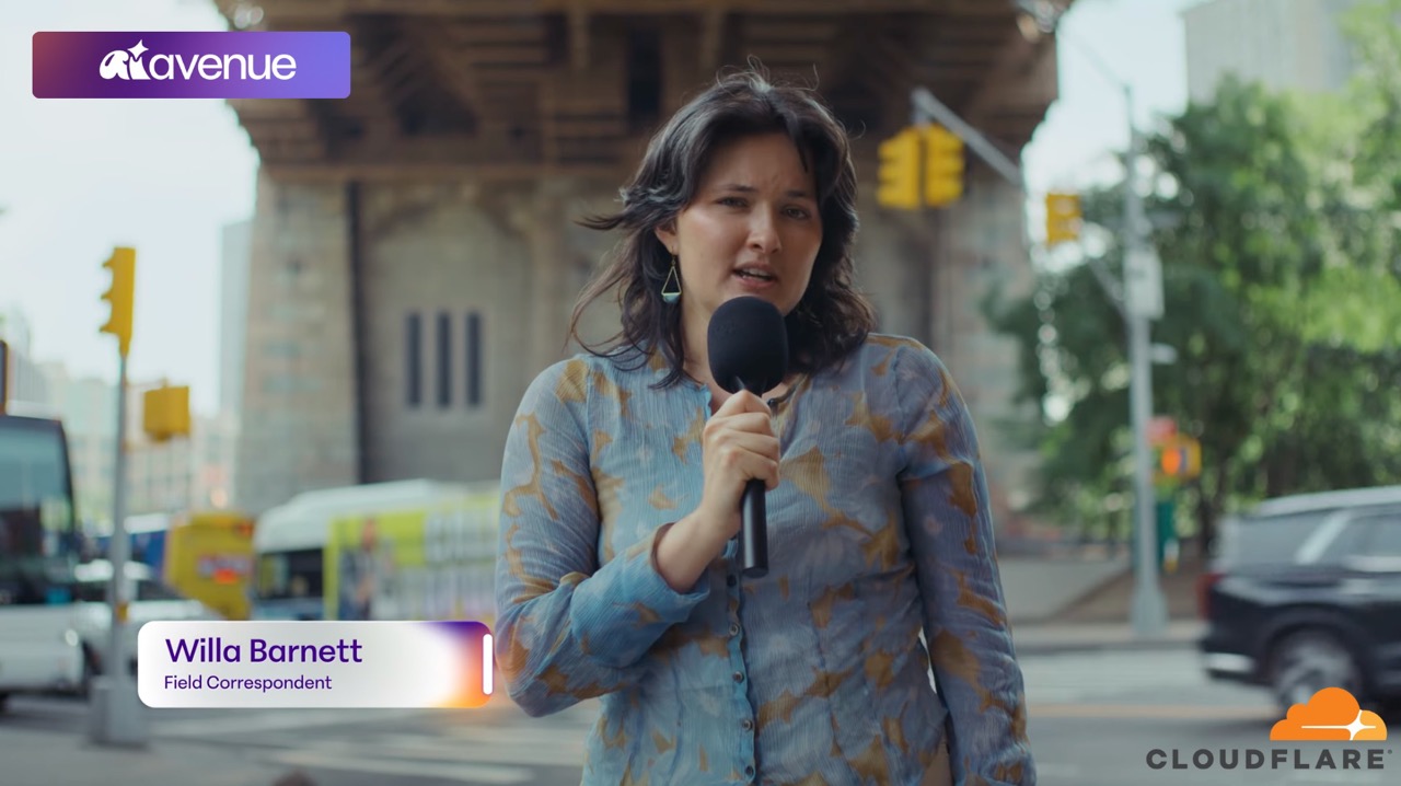 Woman reporter Willa Barnett holding a microphone and speaking on a city street with traffic lights and vehicles in the background.