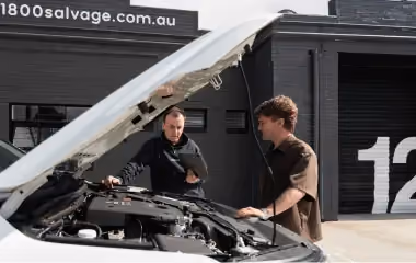 Mechanic inspecting a car engine with the owner at an 1800 Salvage workshop.