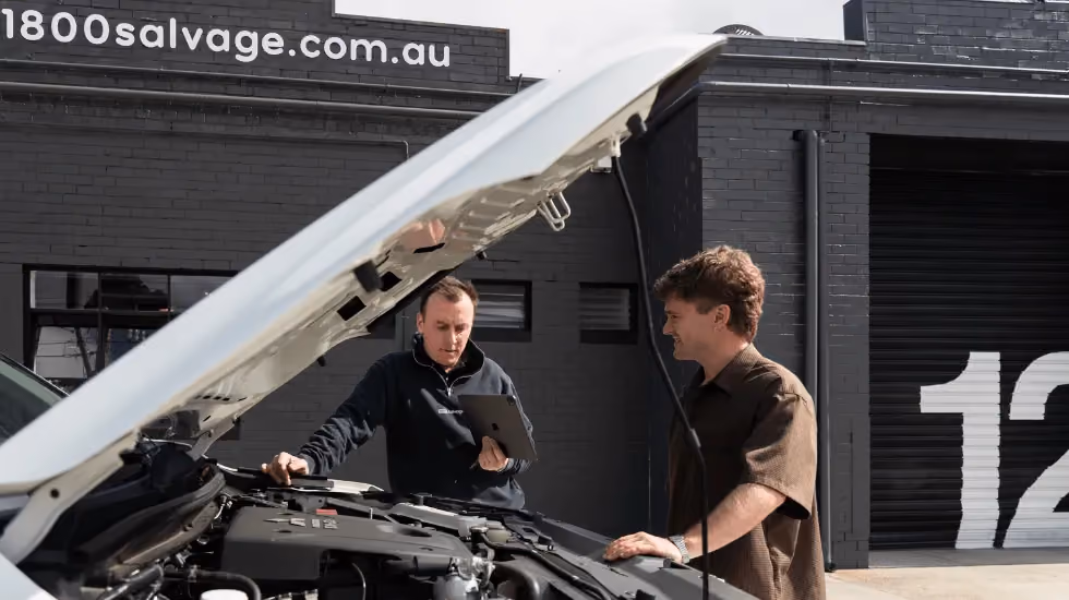 Mechanic inspecting a car engine with the owner at an 1800 Salvage workshop.