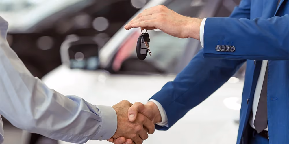 Closeup of a car dealer's hands as he hands over the keys to a new car to his client.