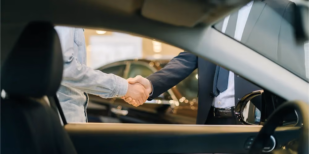 Car dealer and his client shaking hands in a dealership.