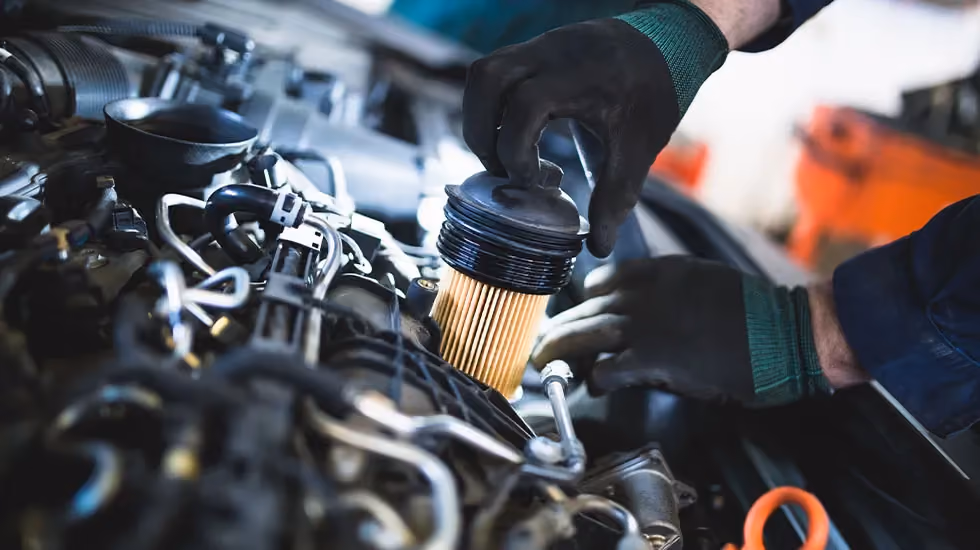 A closeup of a mechanic’s hands as they pull out a car’s oil filter. The more oil your engine has burned, the greater the damage will be. The oil can ruin several critical components, including spark plugs and catalytic converters — it can even destroy the engine entirely.