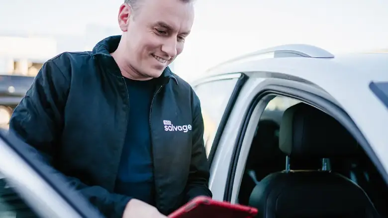 Licensed car buyer from 1800 Salvage in Canberra using a tablet to confirm car details and provide a competitive offer during the selling process.