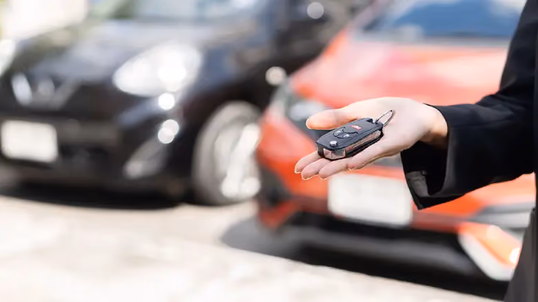 Hand holding car keys in front of parked vehicles, symbolising selling a used car in Adelaide.