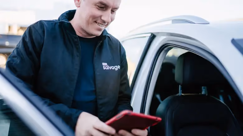 1800 Salvage staff member using a tablet while inspecting an unregistered car in Hobart before collection.