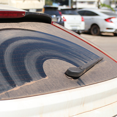 Curved windshield wiper on car rear window with blurry parking lot background