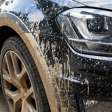 Muddy SUV with splattered dirt on wheel and body after off-road driving