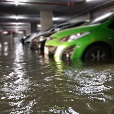 Green car partially submerged in flooded underground parking garage