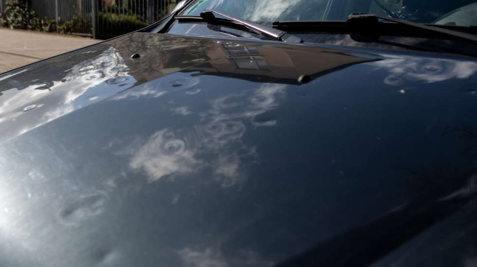 Car hood with hail damage showing multiple dents and reflections