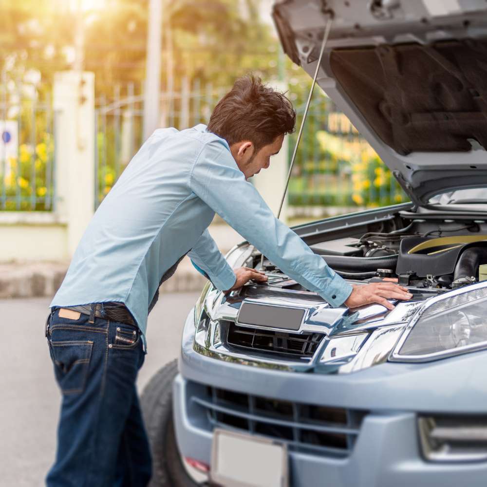 Person checking car engine under open hood on sunny day