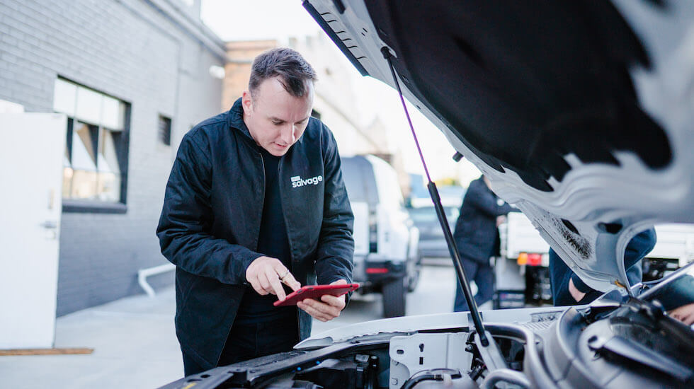 Mechanic in black jacket checking car engine with open hood