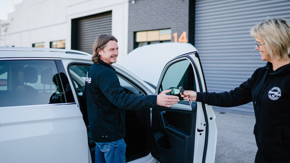 Car rental employee handing over keys to customer in front of white vehicle