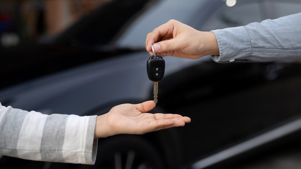 Hand passing car key to another hand in front of vehicle