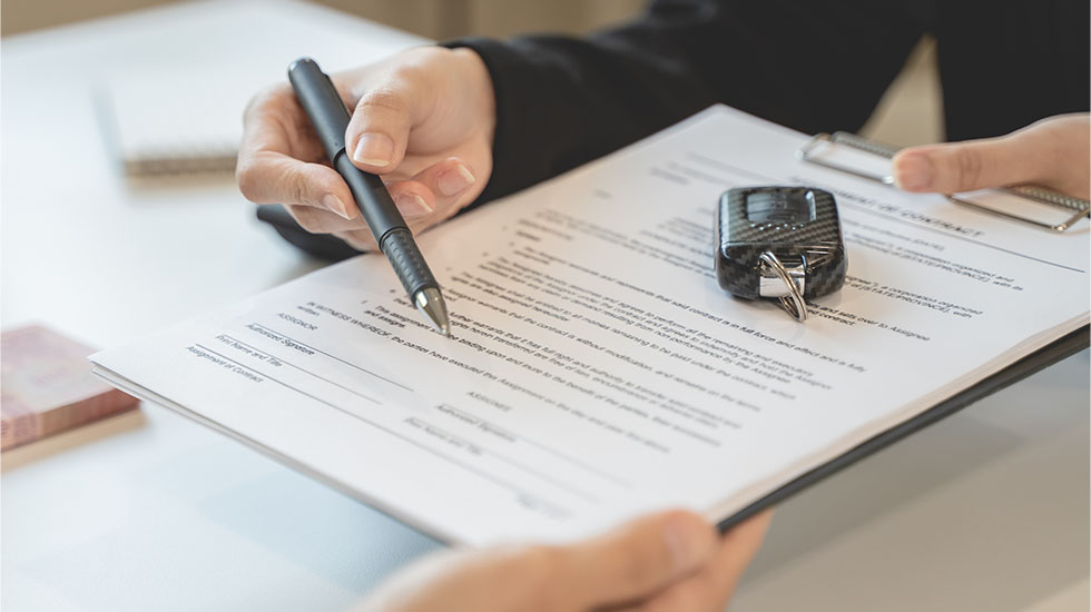 Person signing document with pen and key on desk