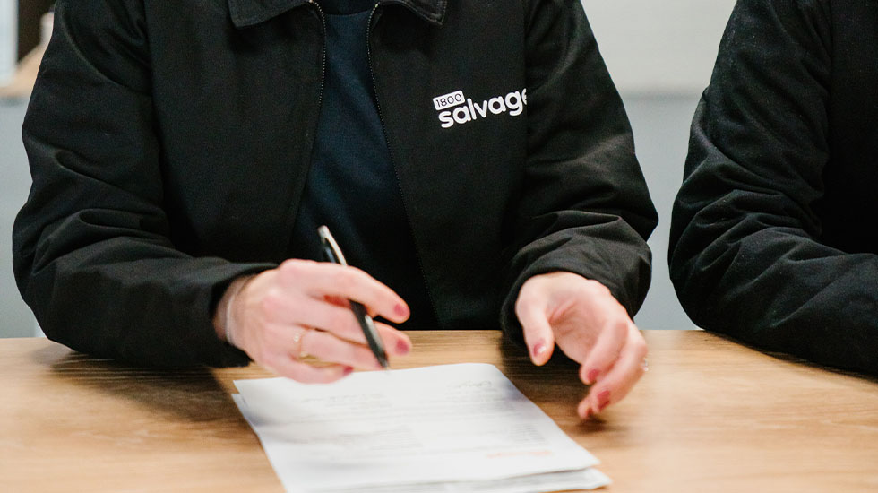 Person in Salvage jacket writing on paper at wooden desk