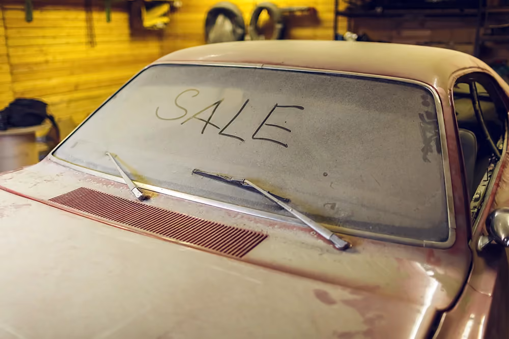 A dusty vintage car with the word 'SALE' written on its windshield,