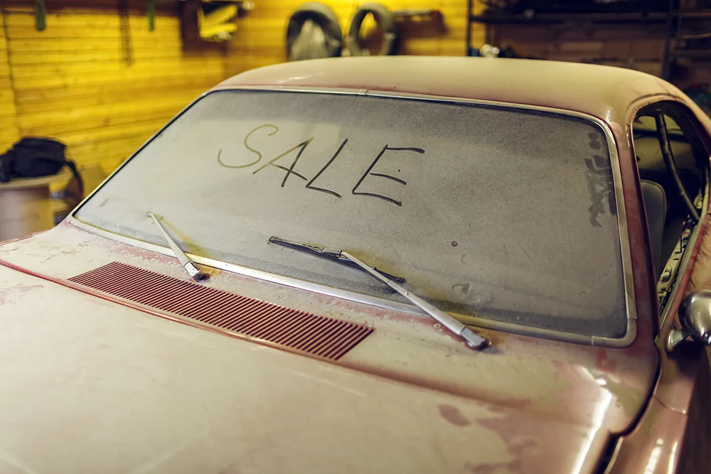 A dusty vintage car with the word 'SALE' written on its windshield,