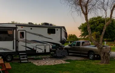 A person holding a roadworthy certificate in front of a parked camper trailer.