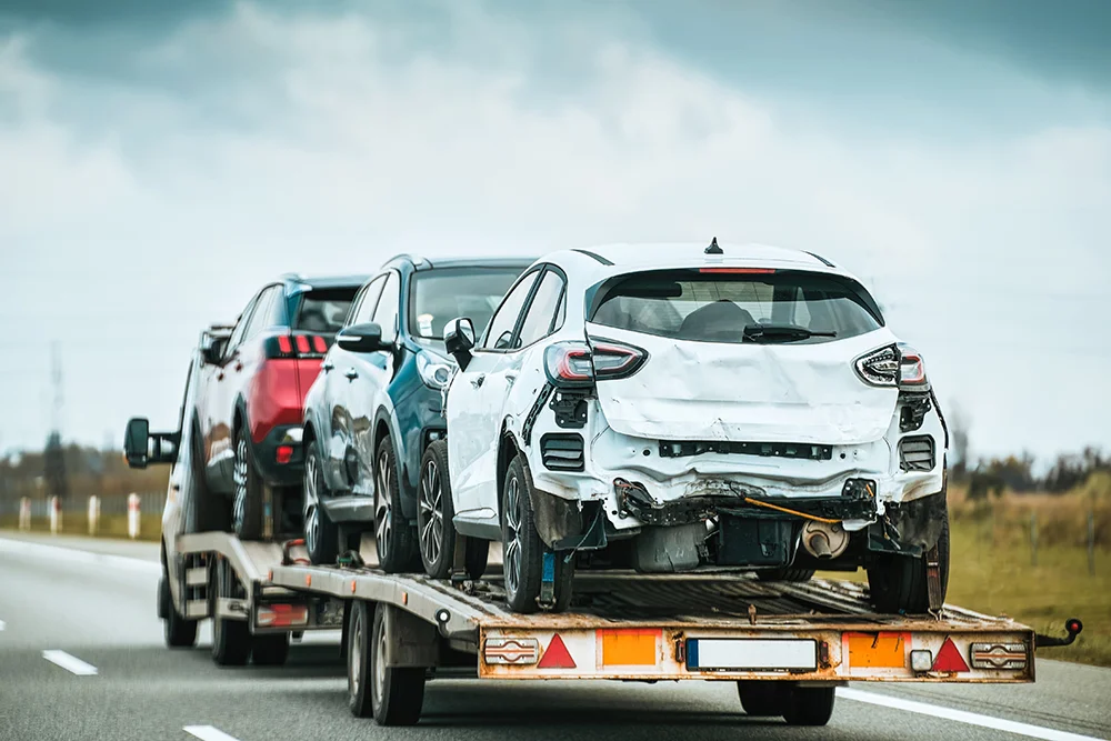 Three damaged cars loaded on a flatbed trailer being transported on a highway