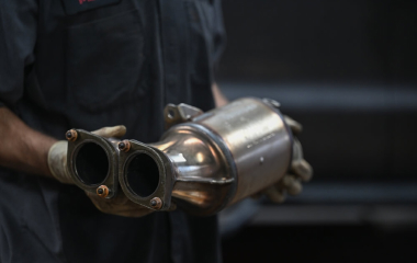 A mechanic holding a catalytic converter, which is a very valuable scrap car part.