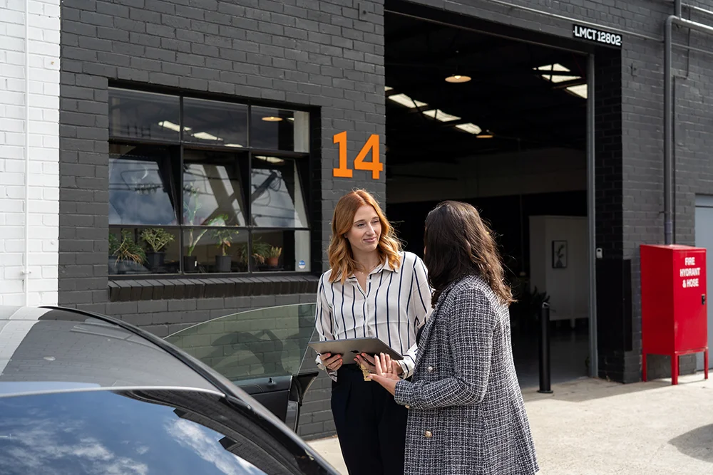 Two woman talking beside a car