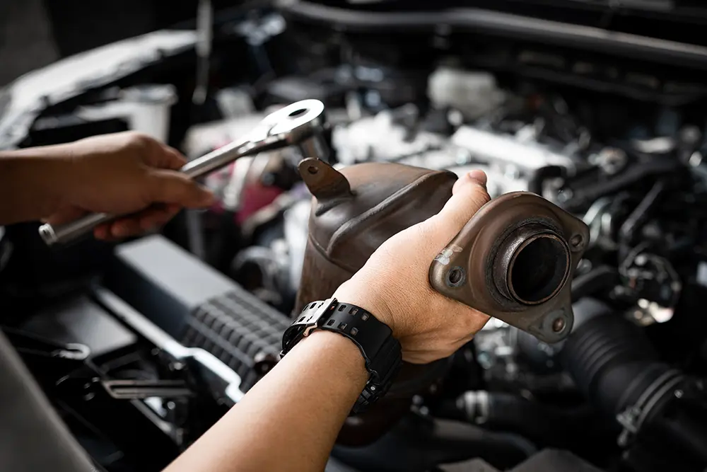 Closeup of a person’s hands as they use a torque wrench to remove an old catalytic converter.