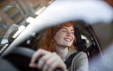 A young woman smiling behind the wheel of a second-hand car she’s just bought.