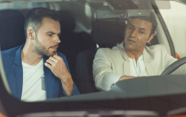 A car owner and a car buyer sitting in the front seats of a second-hand car, looking over its features.