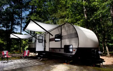 Smiling man handing over keys while an old white camper trailer is being towed away on a flatbed truck in a sunny outdoor setting.