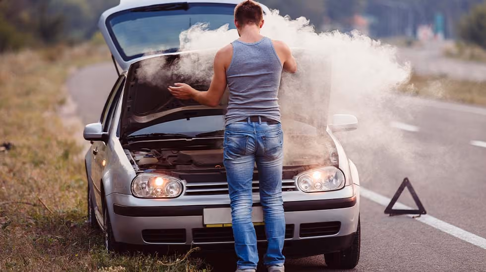 Stranded on the side of the road, a man stares at the smoke billowing out of his car’s engine. 