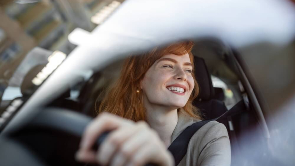 A young woman smiling behind the wheel of a second-hand car she’s just bought.