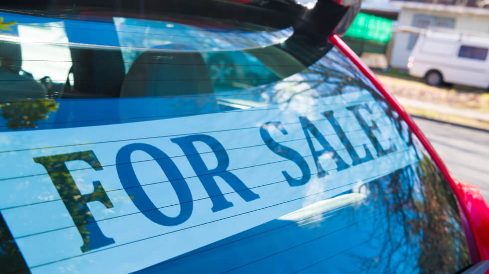 A ‘for sale’ sign stuck to the rear window of a red hatchback car in Sydney.